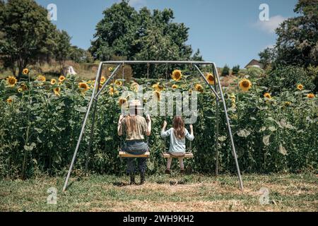 Image fantaisiste de deux sœurs sur une balançoire profitant de l'été dans un champ de tournesols magiques Banque D'Images