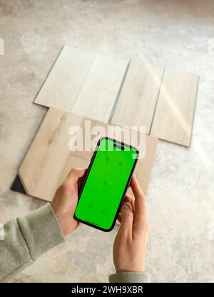 Dispositif de maintien des mains avec écran à touches chromé vert au-dessus des échantillons de bois de vinyle de luxe, stratifié sur le sol dans la maison. Choisir, sélectionner revêtement de sol étanche Banque D'Images