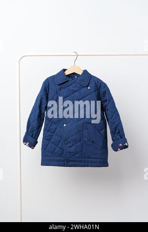 Manteau bleu matelassé pour enfants sur cintre contre mur blanc Banque D'Images