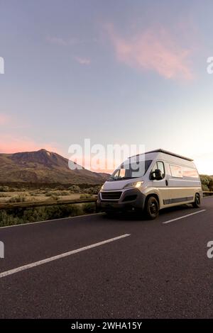 Une camionnette blanche est garée sur le côté d'une route pittoresque, entourée de paysages naturels avec des montagnes en arrière-plan sous un ciel légèrement éclairé au twil Banque D'Images