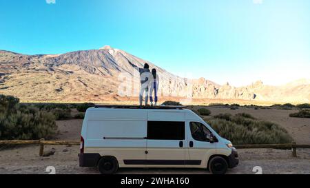 Deux individus debout au sommet d'un van dans le désert, capturés depuis une vue de drone dans la montagne du volcan Teide, Tenerife. Banque D'Images