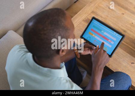 Jeune homme afro-américain examine les données sur une application de maison intelligente sur la tablette à la maison Banque D'Images