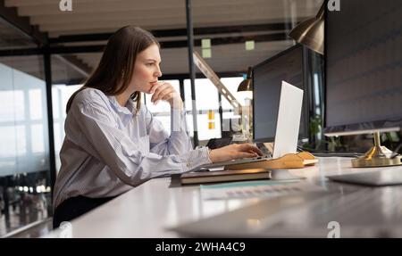 Jeune femme caucasienne travaille intensément à son bureau dans un environnement d'affaires décontracté Banque D'Images