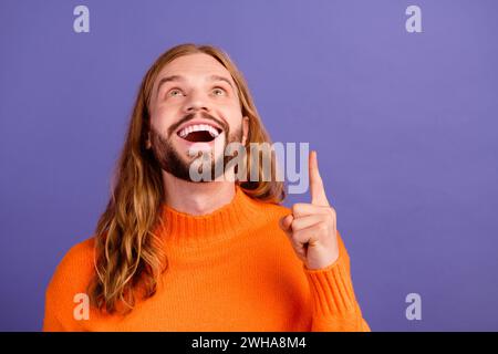 Portrait jeune homme de cheveux blonds portant un pull élégant orange pointant doigt vers le haut étonné regardant bannière isolé sur fond de couleur violette Banque D'Images