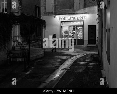 Arles, France - 7 mars 2023 : rue vide dans le centre d'Arles (France) dans la nuit, femme devant la boulangerie, noir et blanc Banque D'Images