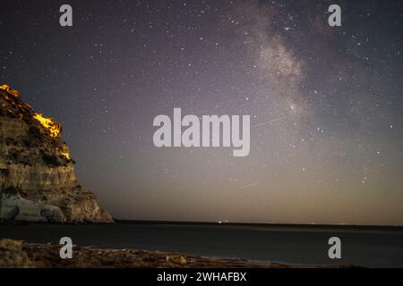 Une scène côtière à couper le souffle où la voie Lactée orne le ciel nocturne sur la mer et la montagne, créant une merveille sereine et cosmique. Banque D'Images