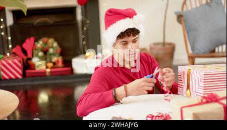 Jeune homme biracial enveloppant des cadeaux à la maison, avec espace de copie Banque D'Images