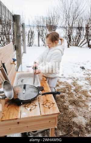 Fille créative avec de la neige dans la cuisine de boue extérieure Banque D'Images