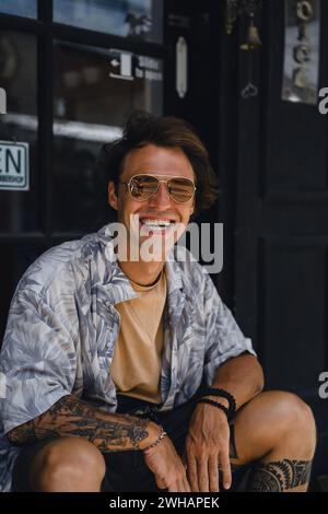Jeune homme beau, romantique, riant avec des lunettes de soleil jaunes. Banque D'Images