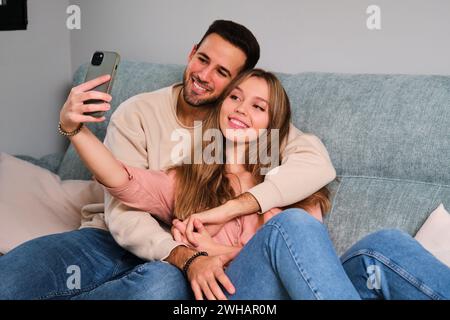 Espagnol couple heureux prenant un selfie ensemble sur un canapé à la maison. Banque D'Images
