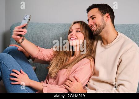 Espagnol couple heureux prenant un selfie ensemble sur un canapé à la maison. Banque D'Images