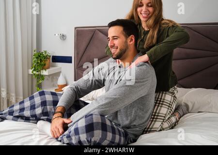 Femme souriante massant les épaules de son petit ami au lit. Banque D'Images