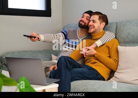 Couple heureux homosexuel regardant la télévision, allumant avec la télécommande. Banque D'Images