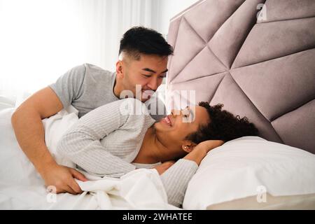 Couple romantique multiracial se réveillent ensemble dans le lit pendant la lune de miel. Banque D'Images