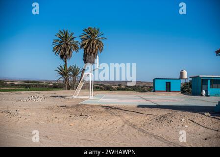 Terrain de basket isolé et abandonné dans une oasis près de Nazca avec des bâtiments de couleur turquoise et ciel bleu avec des palmiers Pérou Banque D'Images