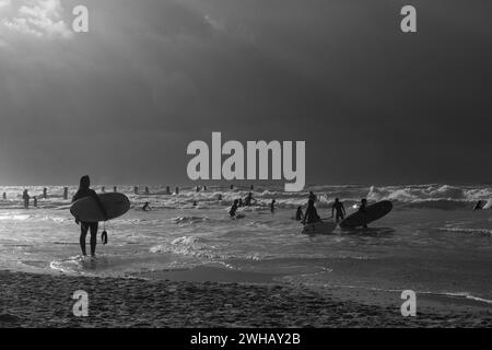 Amateurs de sports nautiques avec diverses formes de surf et de voile en noir et blanc au crépuscule photographiés à la plage de Beit Yanai, Israël Beit Yanai Banque D'Images