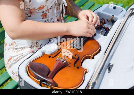 vue de dessus méconnaissable jeune artiste femme portant une robe et assise sur un banc en bois dans le parc sur la rue dézippant violon de cas pour le sortir. copier Banque D'Images