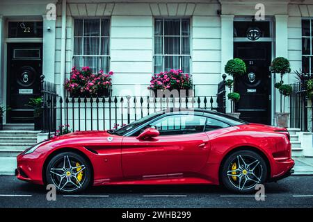 Une Ferrari rouge élégante garée dans une rue classique de Londres, juxtaposant luxe moderne et charme urbain historique. Banque D'Images