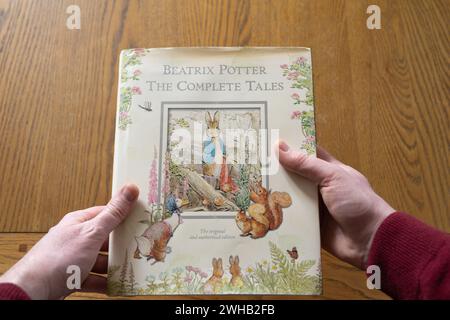 Les mains d'un homme tenant une copie rigide des contes complets de Beatrix Potter, la version originale et autorisée, y compris Peter Rabbit Stories Banque D'Images