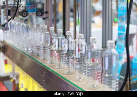 Image montrant une rangée de bouteilles d'eau en plastique transparent sur un tapis roulant dans une usine d'embouteillage, avec un accent particulier sur les bouteilles et les machines industrielles i. Banque D'Images