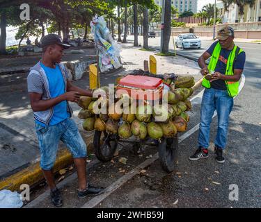 Un jeune immigrant haïtien vend de la noix de coco fraîche dans son chariot près d'une rue animée à Saint-Domingue, en République dominicaine. Banque D'Images