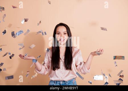 Photo de fille drôle ravie avec cheveux droits porter chemise rose attrapant confettis volants à la partie isolée sur fond de couleur pastel Banque D'Images