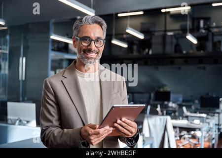 Homme d'affaires mûr souriant dirigeant debout dans le bureau avec tablette. Portrait Banque D'Images
