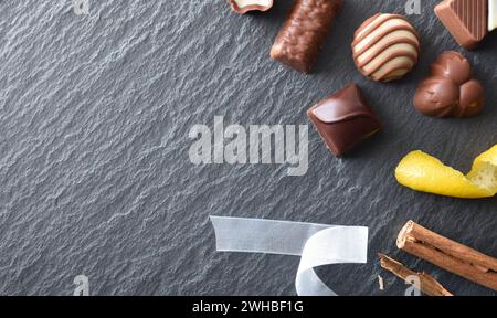 Plusieurs chocolats assortis sur une assiette en ardoise avec des bâtonnets de cannelle et du citron pour la décoration. Vue de dessus. Banque D'Images