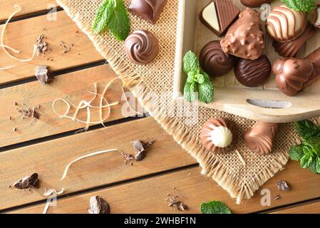 Assortiment de chocolats noirs et au lait issus de l'agriculture biologique sur plateau en bois sur toile de jute sur table en bois avec feuilles de menthe et morceaux de chocolat à l'extérieur Banque D'Images