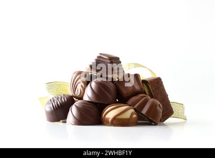 Assortiment avec pile de bonbons au chocolat noir et au lait reflétés sur une table blanche avec ruban doré et fond isolé blanc. Vue de face. Banque D'Images