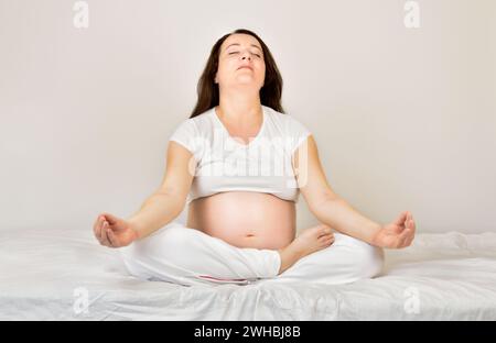Plan d'une femme enceinte méditant sur un tapis d'exercice à la maison Banque D'Images