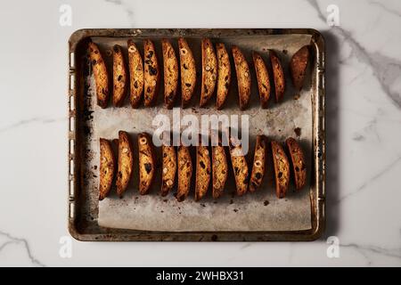 Biscotti aux amandes et aux canneberges fraîchement cuits sur une plaque de cuisson parchemin, vue sur le marbre Banque D'Images