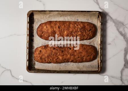 Biscotti aux amandes et aux canneberges fraîchement cuits sur une plaque de cuisson parchemin, vue sur le marbre Banque D'Images