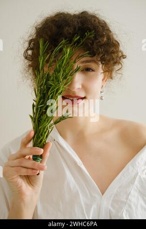 Mignonne jeune femme couvre son œil avec une branche de romarin Banque D'Images