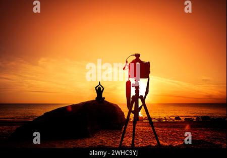 Appareil photo avec trépied devant un coucher de soleil en bord de mer, femme, yoga Banque D'Images