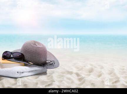 Livre, lunettes de soleil, serviette et chapeau de soleil sur une plage de sable Banque D'Images