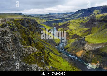 Femme randonneur appréciant les Highlands d'Islande.Rivière Fossa ruisseau dans la vallée du canyon de Landmannalaugar.Les collines et les falaises sont couvertes de mousse verte. Banque D'Images