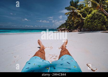 Homme portant un short de natation avec des jambes bronzées sur Paradise sable blanc tropical plage exotique avec vue sur bleu turquoise océan. Voyage vacances concept de vacances. Banque D'Images