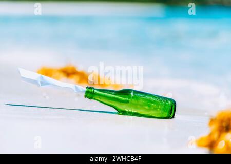 Bouteille verte avec message papier sur la plage de sable blanc avec lagon bleu en arrière-plan. Banque D'Images