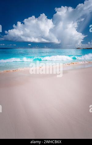 Belle vague de ocen blanc qui se déforme vers la plage de sable tropical. Nuages moelleux au-dessus de la mer bleue. Grande Anse, Seychelles. Banque D'Images