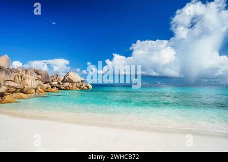 Journée ensoleillée et lumineuse à la plage de la grande Anse, sur l'île de la Digue aux Seychelles. Plage de sable avec baie bleu de l'océan, nuages blancs en arrière-plan. Banque D'Images