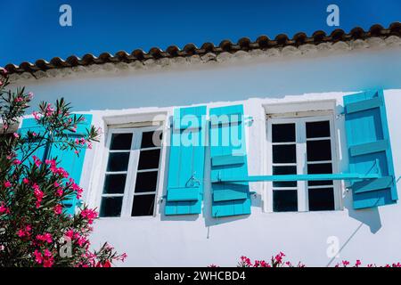 Blanc grec traditionnel avec volet de fenêtre bleu dans le style Mediterraneanstyle et fleurs rosa. Fiskardo, île de Céphalonie, Grèce. Banque D'Images