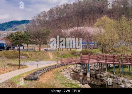 Ruisseau dans le parc public rural avec des bâtiments et des montagnes sous ciel nuageux en arrière-plan Banque D'Images