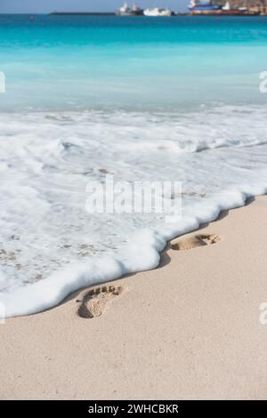 Vagues de l'océan touchant les empreintes de pied sur la plage tropicale. Banque D'Images