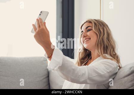 Selfie image de belle et heureuse jeune femme regardant la caméra avec le sourire dentelé. Jolie fille tenant un gadget avec webcam, faisant appel vidéo, auto portrait à la maison. Concept de communication Banque D'Images