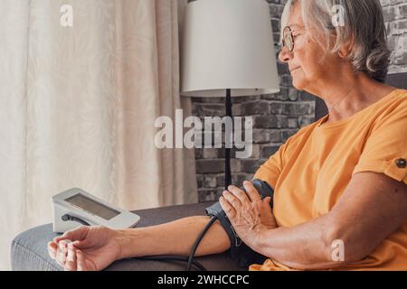 La femme aînée principale mesure l'essai d'hypertension basse pression artérielle tenant à l'aide d'un compteur électronique numérique médical assis sur le canapé à la maison, athérosclérose de maladie cardiaque Banque D'Images