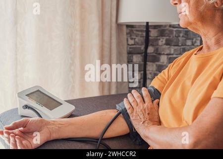 La femme aînée principale mesure l'essai d'hypertension basse pression artérielle tenant à l'aide d'un compteur électronique numérique médical assis sur le canapé à la maison, athérosclérose de maladie cardiaque Banque D'Images