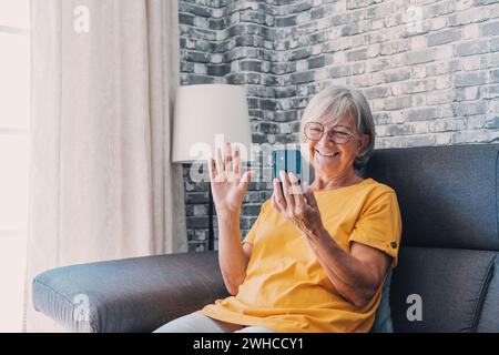 Heureuse dame âgée parlant sur le téléphone portable, faisant appel de la maison, parlant à la famille sur le téléphone portable avec le sourire dentelé. Femme senior des années 70 consultant médecin sur téléphone portable, discutant avec un ami, riant Banque D'Images