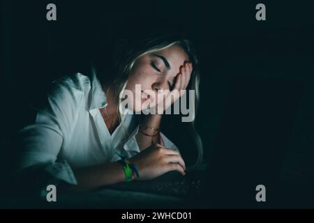 Jeune étudiant caucasien accablé touchant la tête, souffrant d'une vue floue, massant le pont de nez soulageant la douleur, se sentant épuisé travaillant tard dans la soirée sur ordinateur au lit. Banque D'Images