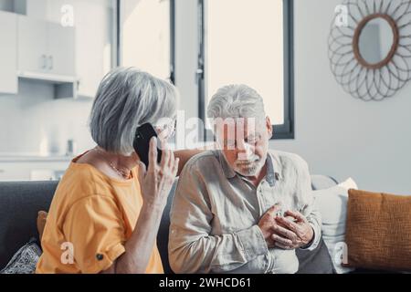 Femme mature, épouse appelant l'urgence, parlant au téléphone, tenant la main du vieux mari, homme aux cheveux gris ayant une crise cardiaque, touchant la poitrine, souffrant de maladie de mal de cœur à la maison, ressentant de la douleur Banque D'Images